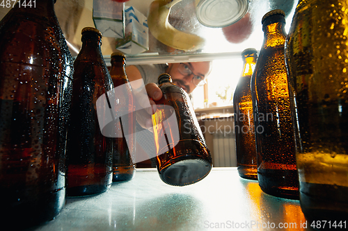Image of Caucasian man takes cold refreshing beer from out the fridge, inside view from fridge of hand holding the bottle