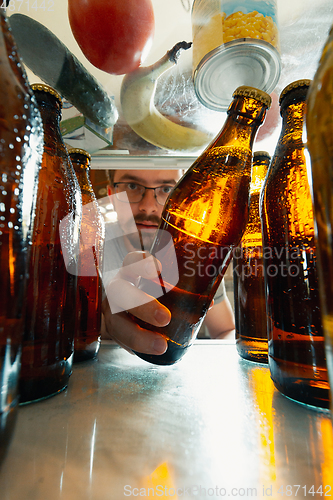 Image of Caucasian man takes cold refreshing beer from out the fridge, inside view from fridge of hand holding the bottle