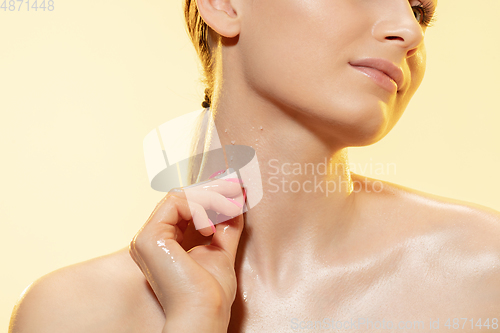 Image of Close up of beautiful woman with melting ice cube over yellow background. Cosmetics and makeup, natural and eco treatment, skin care.