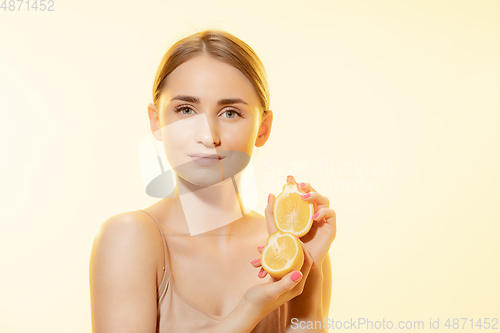 Image of Citrus. Close up of beautiful female face with lemon slices over yellow background. Cosmetics and makeup, natural and eco treatment, skin care.