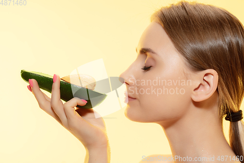 Image of Organic. Close up of beautiful female face with half avocado over yellow background. Cosmetics and makeup, natural and eco treatment, skin care.