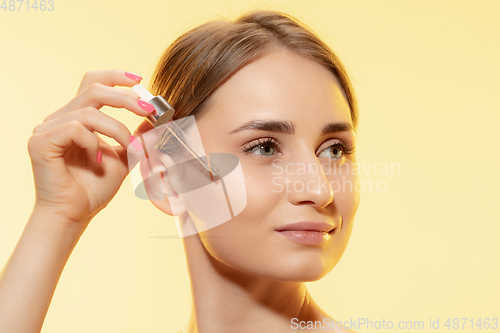 Image of Protection. Close up of beautiful female face with pouring essential oil, serum over yellow background. Cosmetics and makeup, natural and eco treatment, skin care.