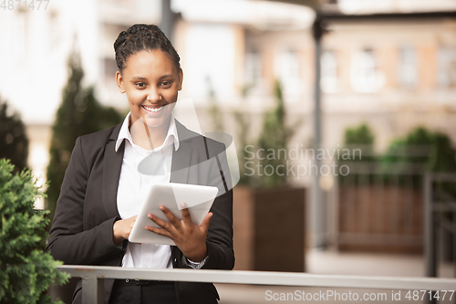 Image of African-american businesswoman in office attire smiling, looks confident and happy, successful