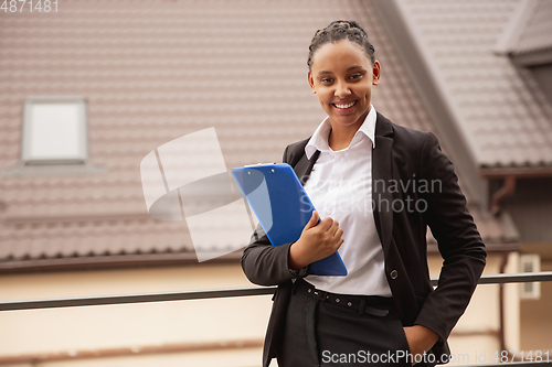 Image of African-american businesswoman in office attire smiling, looks confident and happy, successful