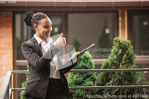 Image of African-american businesswoman in office attire smiling, looks confident and happy, successful