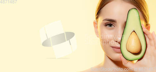 Image of Treatment. Close up of beautiful female face with half avocado over yellow background. Cosmetics and makeup, natural and eco treatment, skin care. Flyer with copyspace.