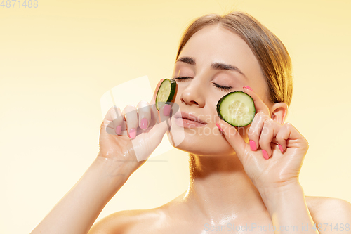 Image of Green. Close up of beautiful female face with cucumber slices over yellow background. Cosmetics and makeup, natural and eco treatment, skin care.