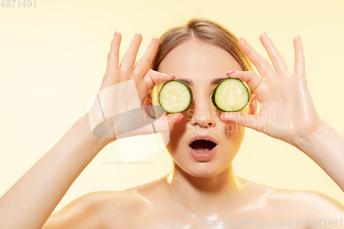 Image of Green. Close up of beautiful female face with cucumber slices over yellow background. Cosmetics and makeup, natural and eco treatment, skin care.