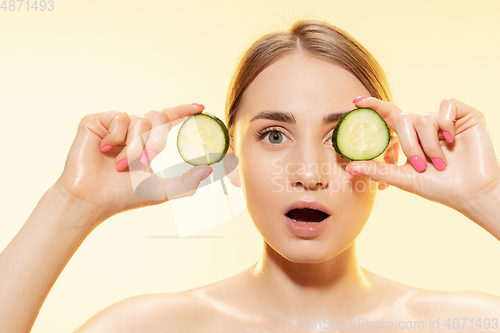 Image of Green. Close up of beautiful female face with cucumber slices over yellow background. Cosmetics and makeup, natural and eco treatment, skin care.