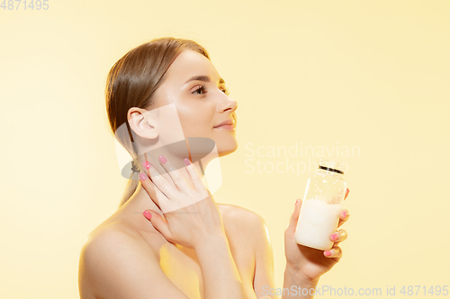 Image of Shining. Close up of beautiful woman with moisturizer over yellow background. Cosmetics and makeup, natural and eco treatment, skin care.