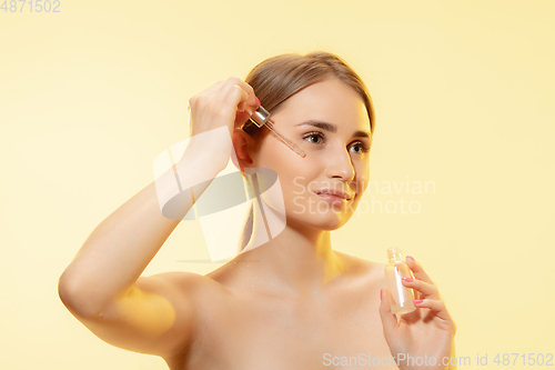 Image of Nutrition. Close up of beautiful female face with pouring essential oil, serum over yellow background. Cosmetics and makeup, natural and eco treatment, skin care.