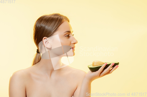 Image of Fresh. Close up of beautiful female face with half avocado over yellow background. Cosmetics and makeup, natural and eco treatment, skin care.