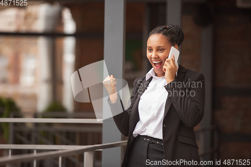 Image of African-american businesswoman in office attire smiling, looks confident and happy, successful