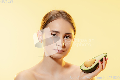 Image of Fresh. Close up of beautiful female face with half avocado over yellow background. Cosmetics and makeup, natural and eco treatment, skin care.