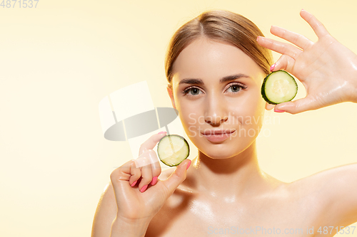 Image of Green. Close up of beautiful female face with cucumber slices over yellow background. Cosmetics and makeup, natural and eco treatment, skin care.