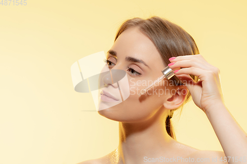 Image of Protection. Close up of beautiful female face with pouring essential oil, serum over yellow background. Cosmetics and makeup, natural and eco treatment, skin care.