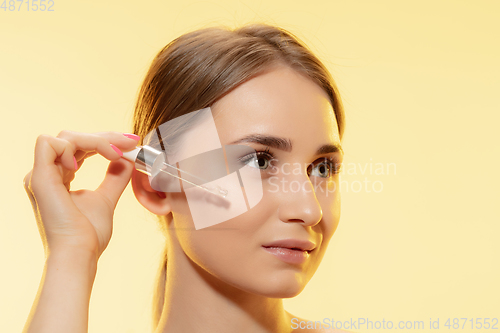 Image of Protection. Close up of beautiful female face with pouring essential oil, serum over yellow background. Cosmetics and makeup, natural and eco treatment, skin care.