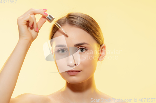 Image of Protection. Close up of beautiful female face with pouring essential oil, serum over yellow background. Cosmetics and makeup, natural and eco treatment, skin care.