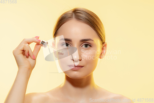 Image of Nutrition. Close up of beautiful female face with pouring essential oil, serum over yellow background. Cosmetics and makeup, natural and eco treatment, skin care.