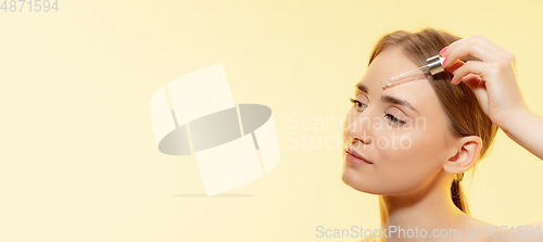 Image of Clear. Close up of beautiful female face with pouring essential oil, serum over yellow background. Cosmetics and makeup, natural and eco treatment, skin care. Flyer with copyspace.