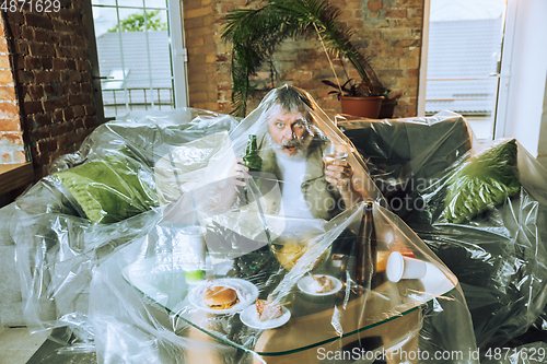 Image of Senior man covered with plastic, eating fast food and drinking beer - environmental pollution by people concept