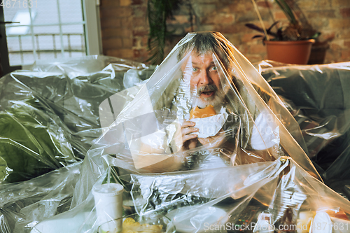 Image of Senior man covered with plastic, eating fast food and drinking beer - environmental pollution by people concept