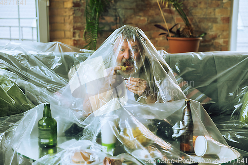 Image of Senior man covered with plastic, eating fast food and drinking beer - environmental pollution by people concept