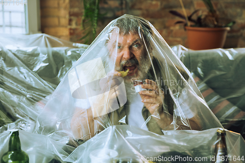 Image of Senior man covered with plastic, eating fast food and drinking beer - environmental pollution by people concept