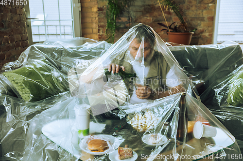 Image of Senior man covered with plastic, eating fast food and drinking beer - environmental pollution by people concept