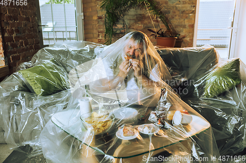 Image of Senior man covered with plastic, eating fast food and drinking beer - environmental pollution by people concept