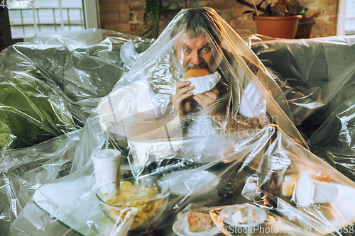 Image of Senior man covered with plastic, eating fast food and drinking beer - environmental pollution by people concept