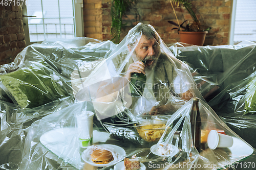 Image of Senior man covered with plastic, eating fast food and drinking beer - environmental pollution by people concept