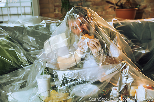 Image of Senior man covered with plastic, eating fast food and drinking beer - environmental pollution by people concept