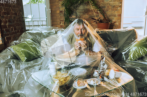 Image of Senior man covered with plastic, eating fast food and drinking beer - environmental pollution by people concept