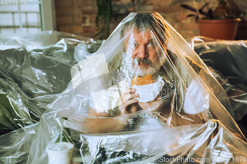 Image of Senior man covered with plastic, eating fast food and drinking beer - environmental pollution by people concept