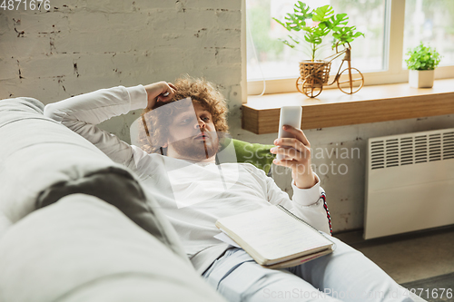 Image of Manager or student working from home while being insulated or keep quarantine \'cause of coronavirus COVID-19. Scrolling phone lying down on sofa.