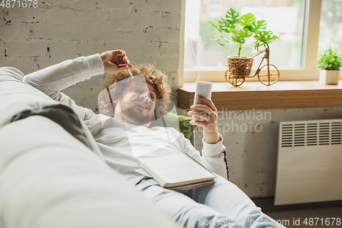 Image of Manager or student working from home while being insulated or keep quarantine \'cause of coronavirus COVID-19. Scrolling phone lying down on sofa.