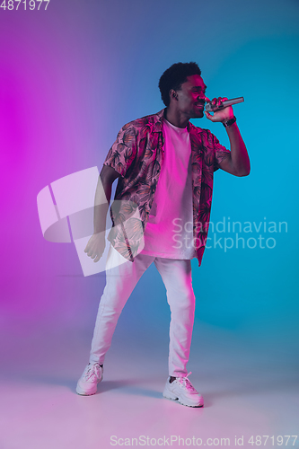 Image of African-american male singer portrait isolated on gradient studio background in neon light