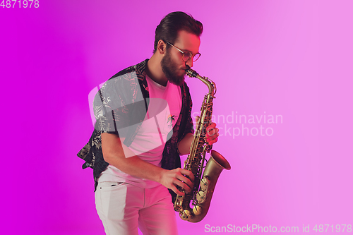 Image of Young caucasian jazz musician playing the saxophone in neon light