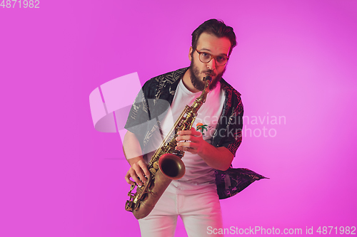 Image of Young caucasian jazz musician playing the saxophone in neon light