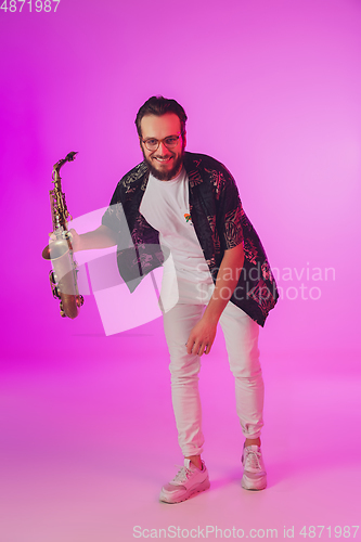 Image of Young caucasian jazz musician playing the saxophone in neon light