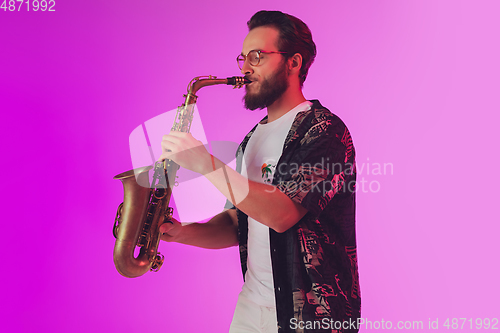 Image of Young caucasian jazz musician playing the saxophone in neon light