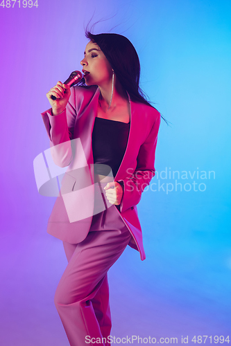 Image of Caucasian female singer portrait isolated on gradient studio background in neon light