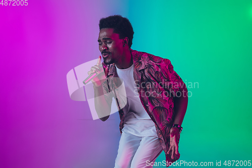 Image of African-american male singer portrait isolated on gradient studio background in neon light