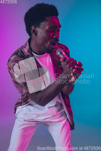 Image of African-american male singer portrait isolated on gradient studio background in neon light