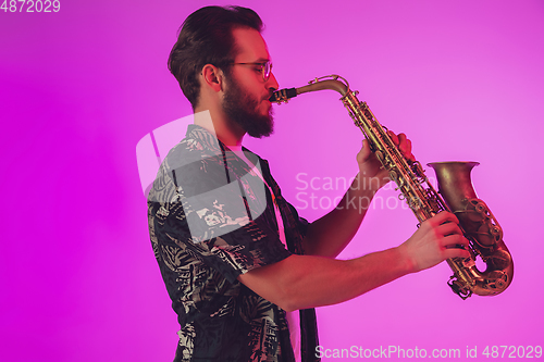 Image of Young caucasian jazz musician playing the saxophone in neon light