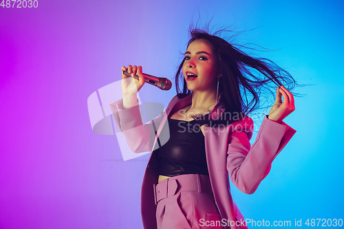 Image of Caucasian female singer portrait isolated on gradient studio background in neon light