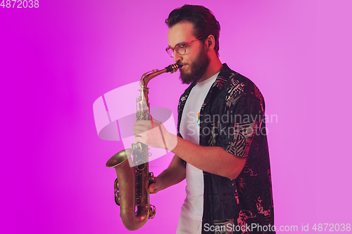 Image of Young caucasian jazz musician playing the saxophone in neon light