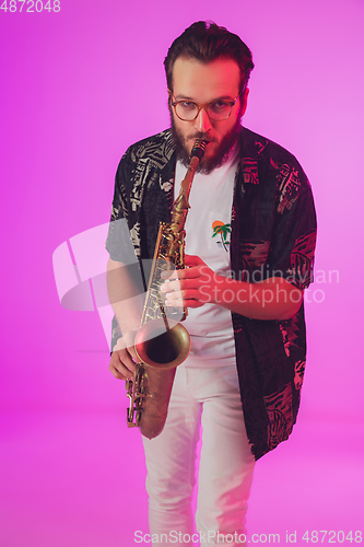 Image of Young caucasian jazz musician playing the saxophone in neon light