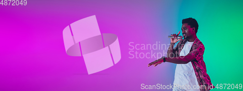 Image of African-american male singer portrait isolated on gradient studio background in neon light, flyer with copyspace
